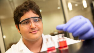 FURI student Dominic Varda looks at beakers of red liquid.