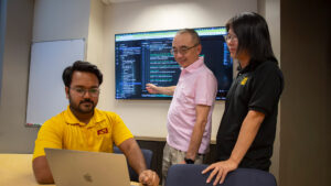 Kumar Satvik Chaudhary types on a laptop while his faculty mentor points at a monitor.