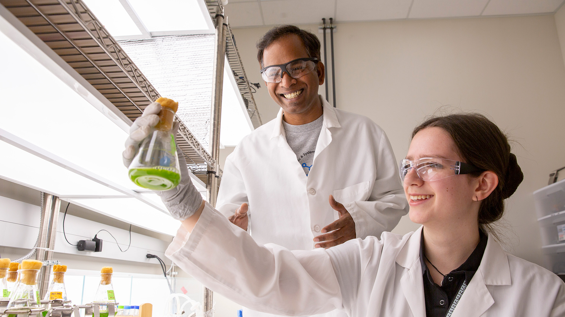 Shira Shecter and her faculty mentor examine green liquid in a flask in a lab.