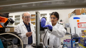Munia Ahmed works with equipment in a lab while her faculty mentor watches.