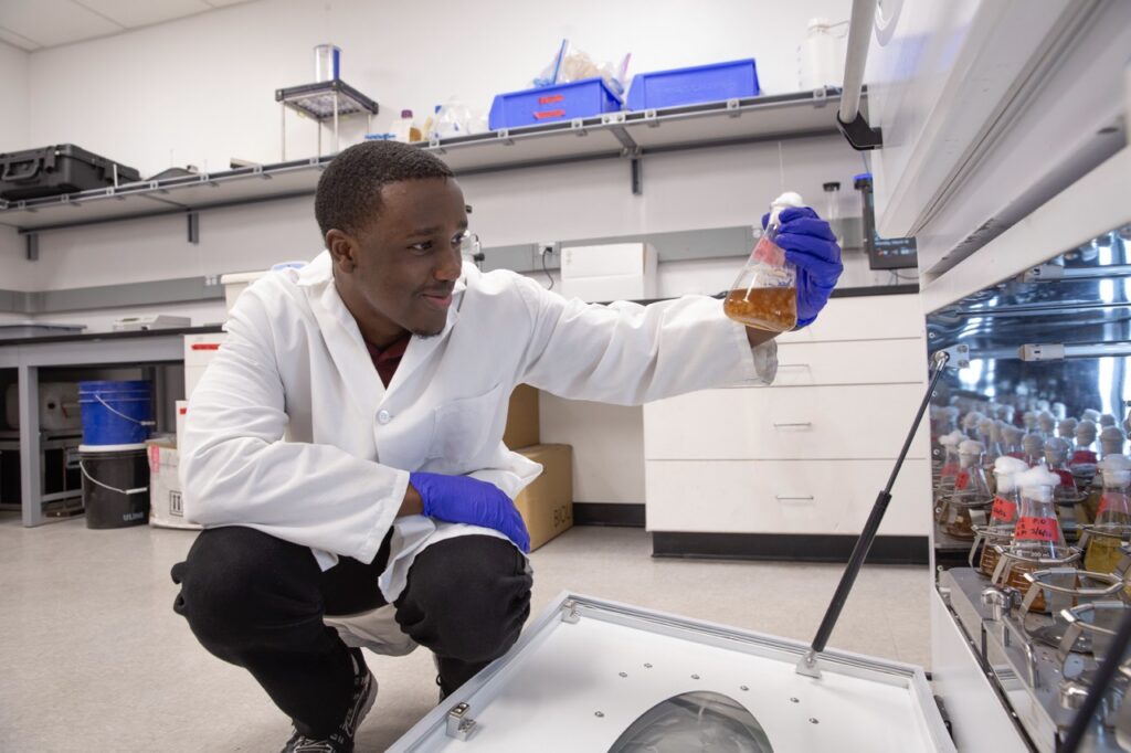 Jamie Magezi holds up a flask of liquid while checking samples in a laboratory incubator.