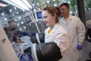 Lia Ryan works inside a glove box while faculty mentor Xin Xu observes in a lab