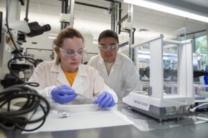Lia Ryan uses tweezers to handle a sample at a lab bench while faculty mentor Xin Xu looks on
